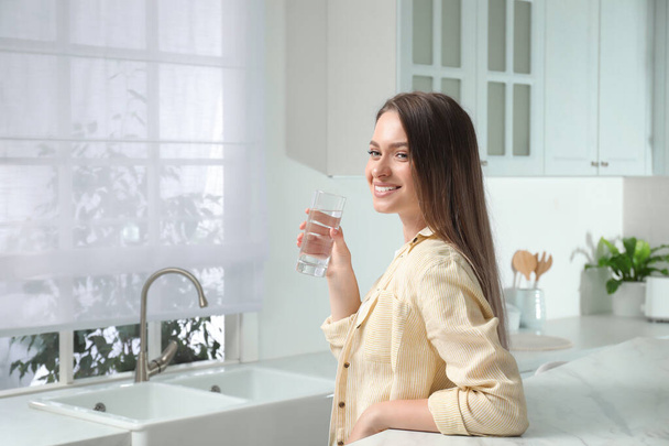 Woman with glass of tap water in kitchen - Valokuva, kuva
