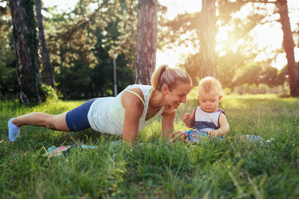 young mother physical exercises with her baby boy outdoor in public park - Fotoğraf, Görsel
