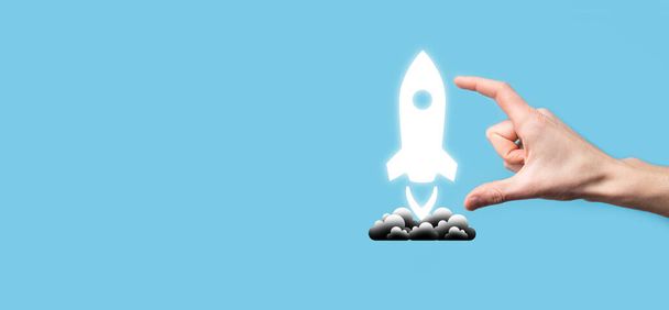 Mužská ruka drží raketu ikonu, která vzlétne, start na modrém pozadí. raketa startuje a odlétá, Business start up, Icon marketing na moderním virtuálním rozhraní.Start up koncept - Fotografie, Obrázek