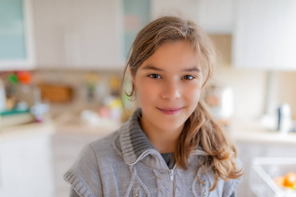 Красива блондинка усміхнена дівчина-підліток у сірому светрі сидить за столом на кухні
. - Фото, зображення
