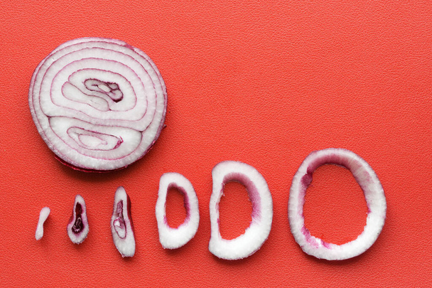 Cebulowe krążki cebuli z czerwonej sałaty leżą na czerwonym tle. Zbliżenie - Zdjęcie, obraz