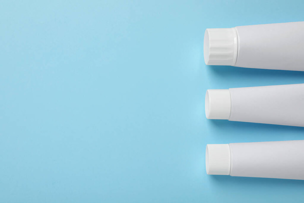 Blank tubes of toothpaste on light blue background, flat lay. Space for text - Fotoğraf, Görsel