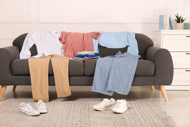 Shoes near sofa with different clothes indoors - Foto, imagen