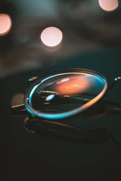 A selective focus of a pair of glasses on a dark surface with a blurry background - Foto, Bild