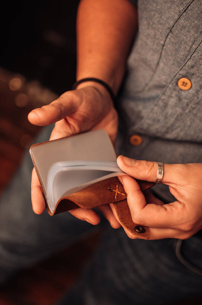 Un primer plano de manos masculinas con un anillo de plata comprobando un pequeño titular de tarjeta de visita vacío marrón - Foto, imagen