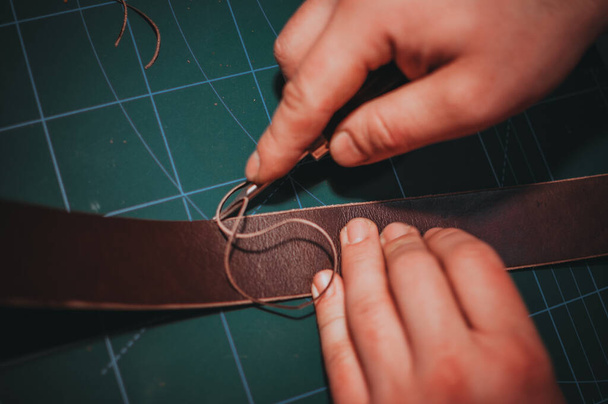 A closeup shot of hands fixing the edges of the brown leather belt by cutting with the sharp knife - Photo, Image