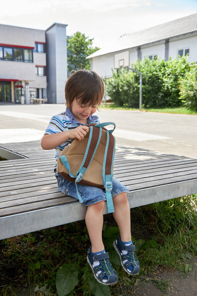 Evlat, Toddler öğle yemeğini, kahvaltısını okul bahçesindeki sırt çantasından alıyor. Okul boyunca ve evin dışında çocuklar için yiyecek. Sağlıklı atıştırmalıklar, ev yapımı yemekler. - Fotoğraf, Görsel
