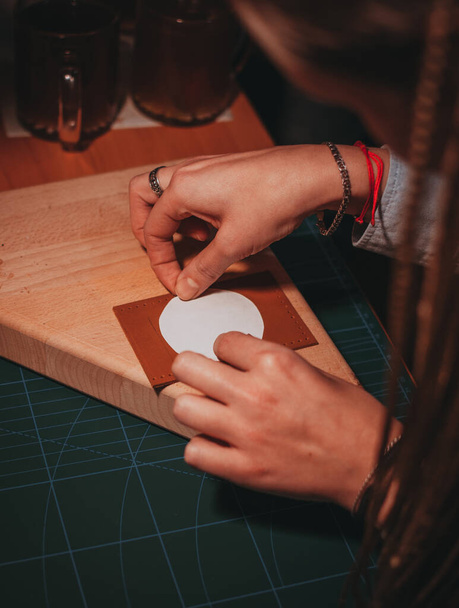 The two hands pressing a white sticker on the leather brown card holder on a wooden surface - Photo, Image