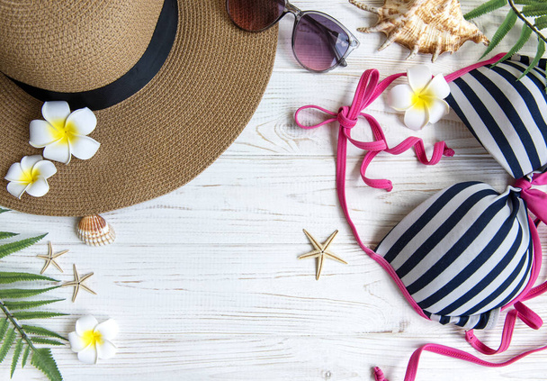 Koncept letních prázdnin. Slaměný klobouk a plážové doplňky s mušlemi a hvězdice na bílém dřevěném pozadí - Fotografie, Obrázek