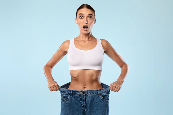 Shocked Skinny Woman Pulling Her Old Large Loose Jeans - 写真・画像