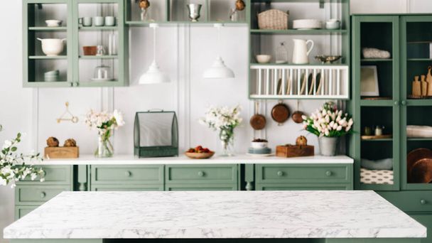 Comptoir en marbre propre et vide, mobilier de cuisine vintage vert avec beaucoup de fleurs et bol de fraises, paire de lumières suspendues blanches, diverses vaisselle en arrière-plan flou - Photo, image
