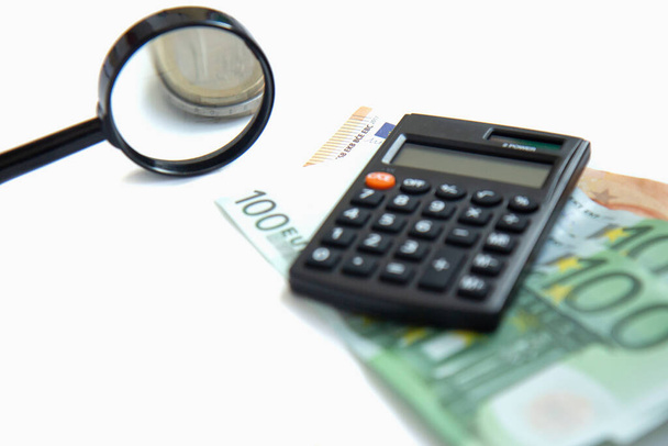 Калькулятор, лупа, бумажные деньги и стопка монет изолированы на белом фоне - Фото, изображение