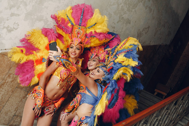 Vrouw in Braziliaanse samba carnaval kostuum met kleurrijke veren verenkleed met mobiele telefoon selfie in oude ingang met groot raam - Foto, afbeelding