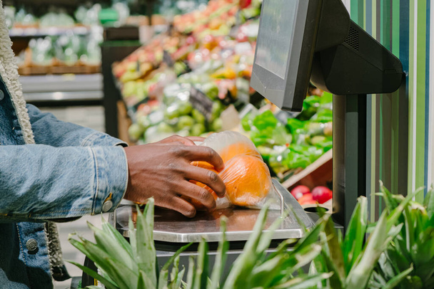 African-American guy in mask weighs oranges in supermarket - Fotografie, Obrázek