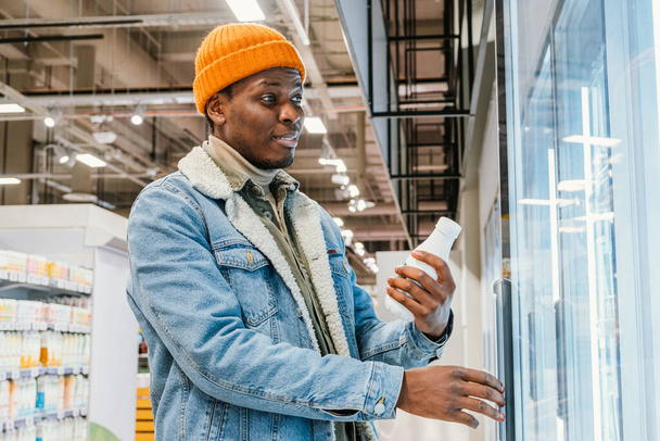 Afroamerykanin bierze mleko z lodówki w supermarkecie. - Zdjęcie, obraz