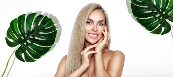 A beautiful young girl in the studio on a white background with flawless and healthy skin holds a large green tropical leaf in hands and covers a part of her face. Fashion, beauty, make-up, cosmetics. - Photo, Image
