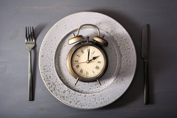 Konzept des intermittierenden Fastens, ketogene Ernährung, Gewichtsverlust. Gabel und Messer auf einem Teller und Wecker - Foto, Bild