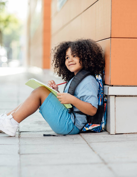 chico guapo que hace su tarea después de la escuela, con un cuaderno y una mochila y pluma, preescolar - Foto, imagen