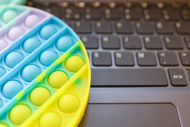 Multicolored antistress silicone Pop it.Toy on the keyboard laptop,pause from work.Sensory toy for kids and adults, antistress.Indoors shot.Businessman or freelancer relaxes playing pop it.closeup. - Photo, Image