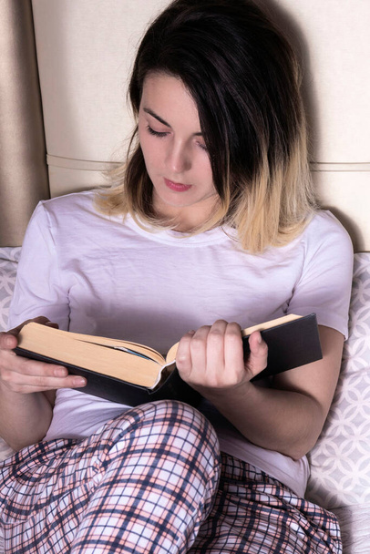 woman reading in bed in a white t-shirt and plaid pajamas - Foto, imagen