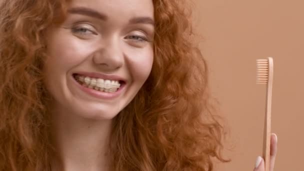 Piros hajú nő pózol gazdaság fogkefe mosolygós kamera, bézs háttér - Felvétel, videó