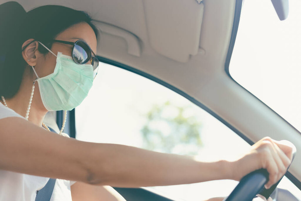 mujer conduciendo coche con máscara médica y gafas de sol en la cara. Asistencia sanitaria y protección contra el virus. - Foto, imagen