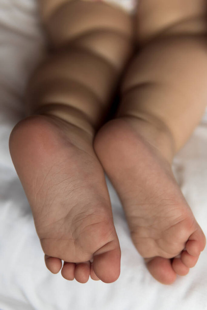 feet of toddler baby girl wearing diapers lying on white bed at home. plump legs of sleeping one year old caucasian child. kid sleeps in crib. home, comfort, childhood, care, love, sweet dream concept - Fotoğraf, Görsel