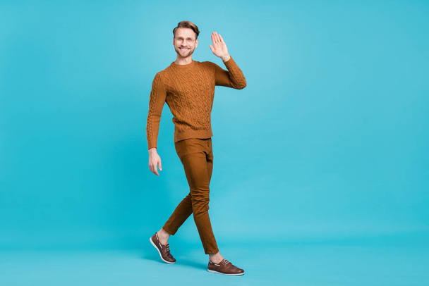 Full body photo charming happy young man walk go empty space wave hello isolated on blue color background - Foto, imagen