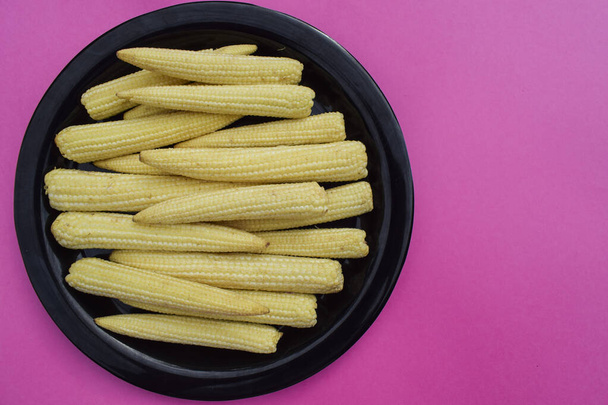 Fresh and organic Babycorn vegetble whole pieces arranged on black plate on pink solid background blank space to write text wallpaper poster - Photo, Image