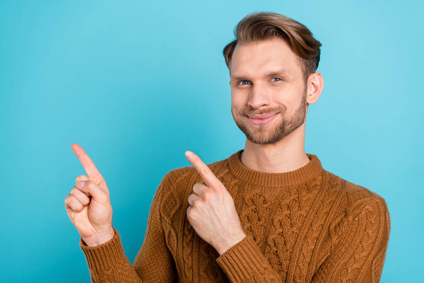 Photo of sweet attractive young guy dressed knit sweater smiling pointing fingers empty space isolated blue color background - Fotografie, Obrázek
