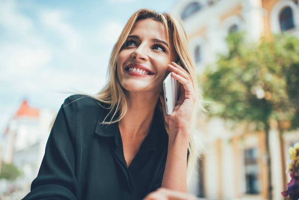 Happy attractive Caucasian female smiling while calling to best friend for making international smartphone conversation, cheerful hipster girl with white teeth enjoying phone talking in roaming - Photo, Image