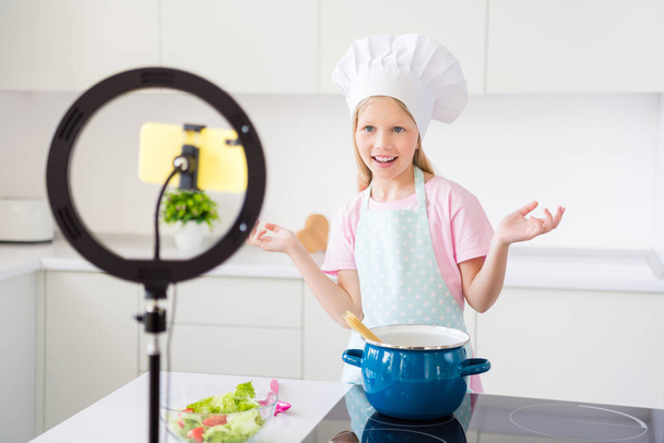Fotografie mladé malé holčičky šťastný pozitivní úsměv říct vlogger nahrávání videa kuchyně jídlo mobilní telefon lampy uvnitř - Fotografie, Obrázek