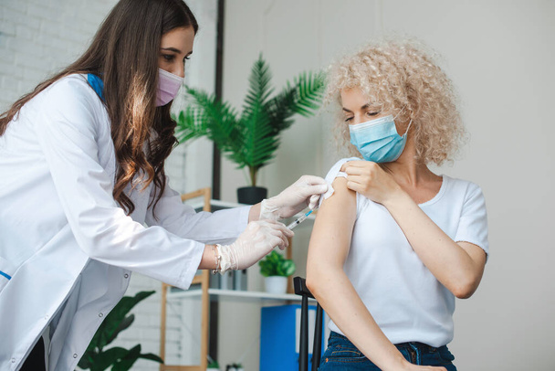 Женщина в медицинской маске ставит вакцину для здоровья концепции. Врач делает пациенту инъекцию коронной вирусной вакцины. Антивирусная вакцина. Ковид19-иммунизация - Фото, изображение