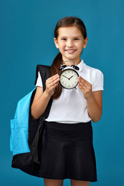 schoolgirl with backpack is holding alarm clock - Фото, изображение