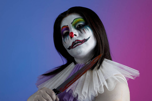 Mujer latina con maquillaje de payaso diabólico, sosteniendo un cuchillo en su mano, tema de Halloween - Foto, imagen