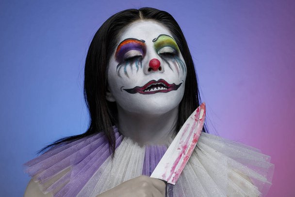 Femme latine avec maquillage de clown diabolique, tenant un couteau dans sa main, thème halloween - Photo, image