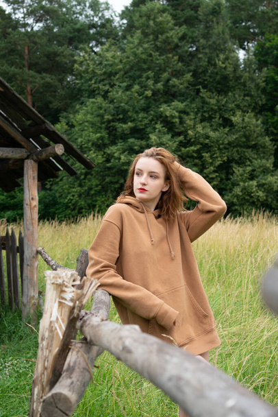 young beautiful woman posing in the summer in a field in a brown sweater - Фото, изображение