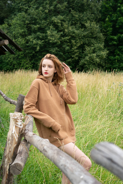 junge schöne Frau posiert im Sommer auf einem Feld in einem braunen Pullover - Foto, Bild