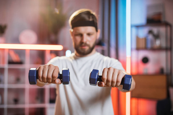 Smiling man in headband using dumbbells for workout at home - Photo, Image