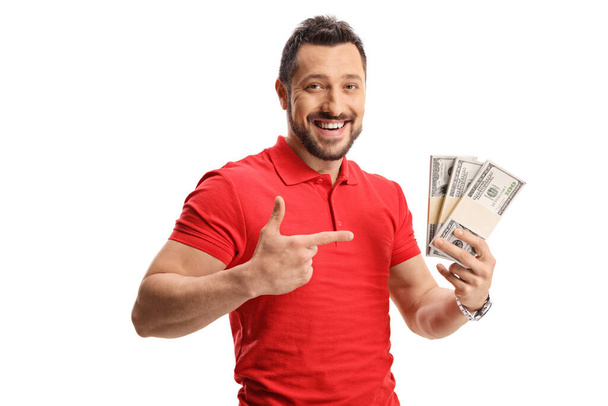 Smiling man in a red t-shirt holding money and pointing isolated on white background - Foto, immagini