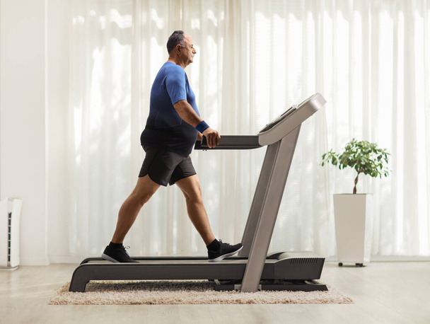 Full length profile shot of a mature man walking on a treadmill inside a room - Foto, afbeelding