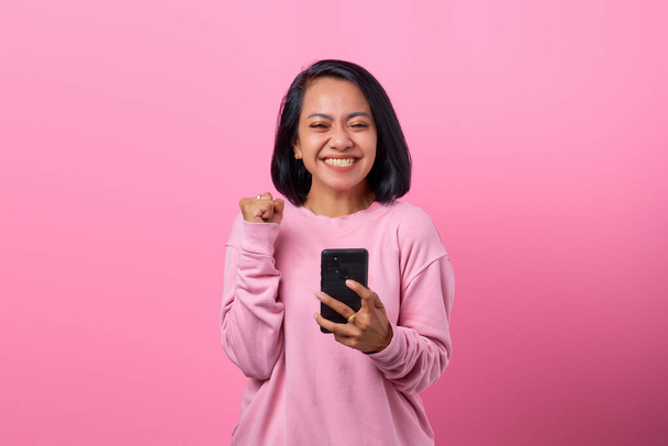 Retrato emocionada joven con teléfono inteligente sobre fondo rosa - Foto, imagen