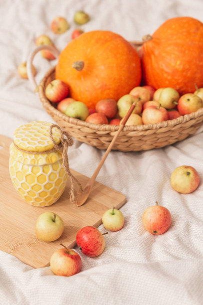 Een pot honing, pompoen en appels in een rieten mandje op een natuurlijke stof. - Foto, afbeelding