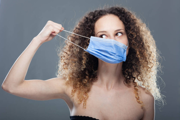Girl with curly hair wearing medical face mask to protect herself viruses, polution or dust. Studio portrait. - Photo, Image