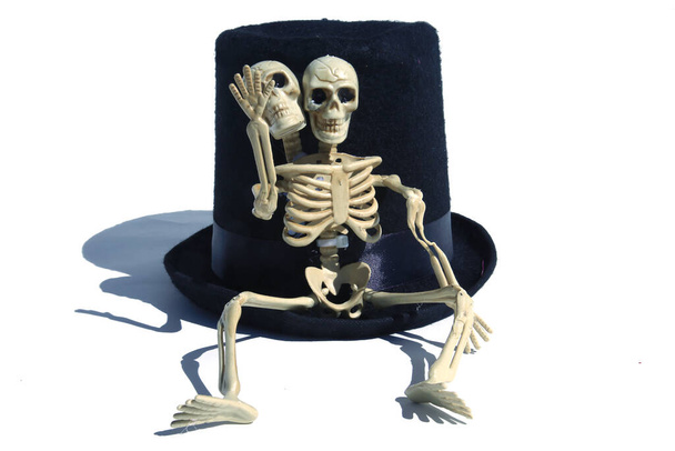 Απόκριες. Δύο Κεφαλές Σκελετός. Μαύρο Top Hat με δύο κεφάλια σκελετό. Καπέλο αποκριάς. απομονωμένο σε λευκό. δωμάτιο για κείμενο. Απόκριες κρανίο φορώντας παλιά στενάχωρο καπέλο. - Φωτογραφία, εικόνα