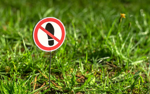 Un panneau rond rayé d'une bande rouge interdisant de marcher sur l'herbe verte. - Photo, image