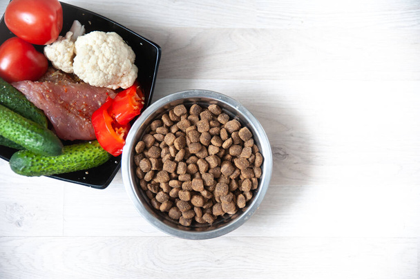 Bowl with dog food, next to natural products, vegetables and meat close-up and space for text, top view. Healthy pet food concept - Φωτογραφία, εικόνα