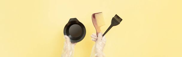 Βούρτσες και μπολ για το σπίτι ή το σαλόνι βαφή μαλλιών στα χέρια μιας γυναίκας με γάντια σε κίτρινο φόντο - Φωτογραφία, εικόνα