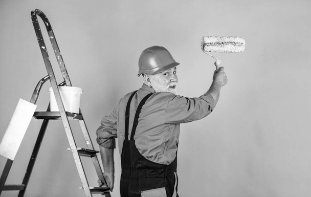 Assistant. Craftsman With Paint Roller. House Painting and Renovation Business. making repair tool. Painter working at construction site. senior man use roller on ladder. work in apartment - Foto, Imagem