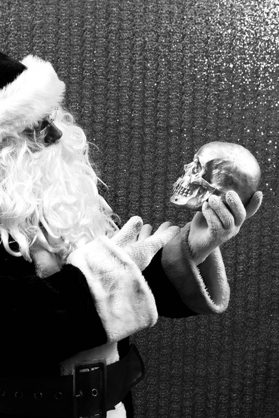 Halloween. Navidad. Santa Claus. Santa Claus sostiene un cráneo humano. Santa encuentra un viejo cráneo de elfo. El viejo Winter está asustado. Le vendí mi alma a Santa. El malvado Santa Claus. Santa o Satanás tú decides. Calavera Malvada de Navidad. Calavera humana con un sombrero de Papá Noel.  - Foto, imagen